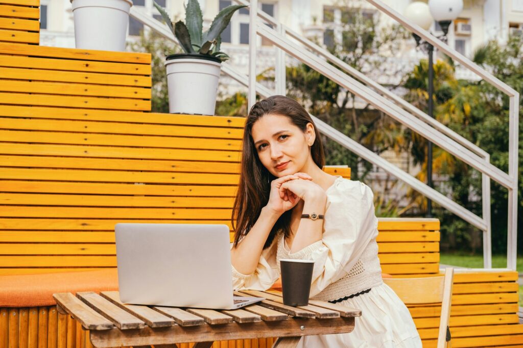 Beautiful caucasian young woman, beige casual dress, sitting at cafe , using laptop. Remote work ad