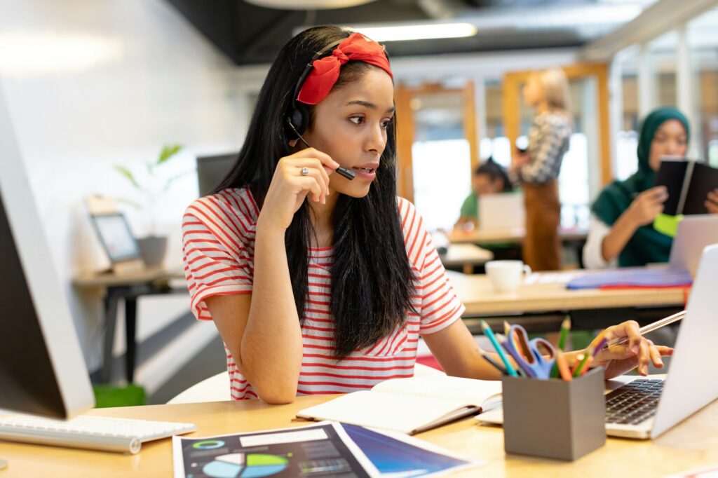 Beautiful Mixed-race female customer service executive talking on headset and working on laptop