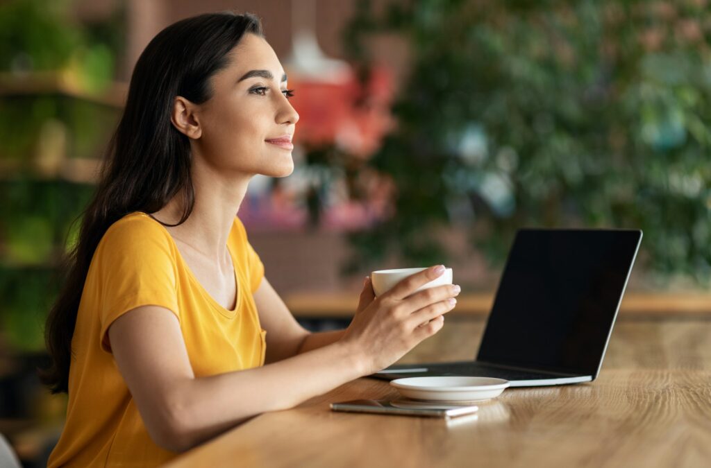 Happy young lady using laptop at cafe