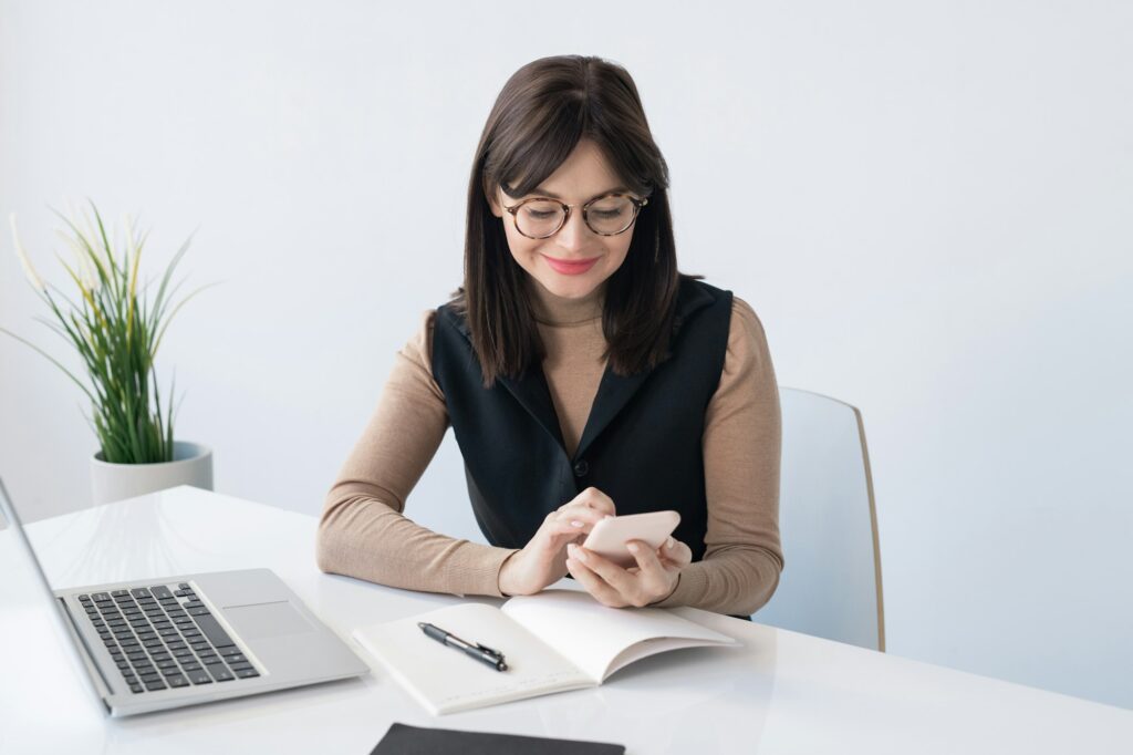 Young teacher or businesswoman with smartphone over open copybook